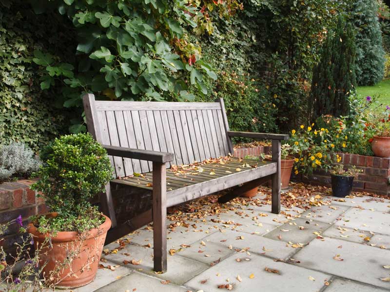 traditional grey limestone patio with timber bench and low brick retainning wall. Patio is dotted with fallen autumn leaves