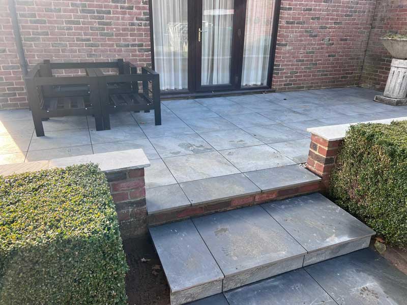 limestone patio adjacent to a house with retaining wall and steps leading down to a lawn