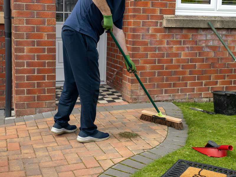 gentleman in blue casual clothing sweeping his front doorstep and path