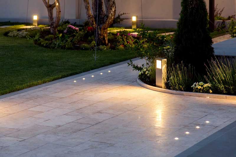 gentle garden lighting provided by recessed lights set into the paving with pillar lights in planting beds