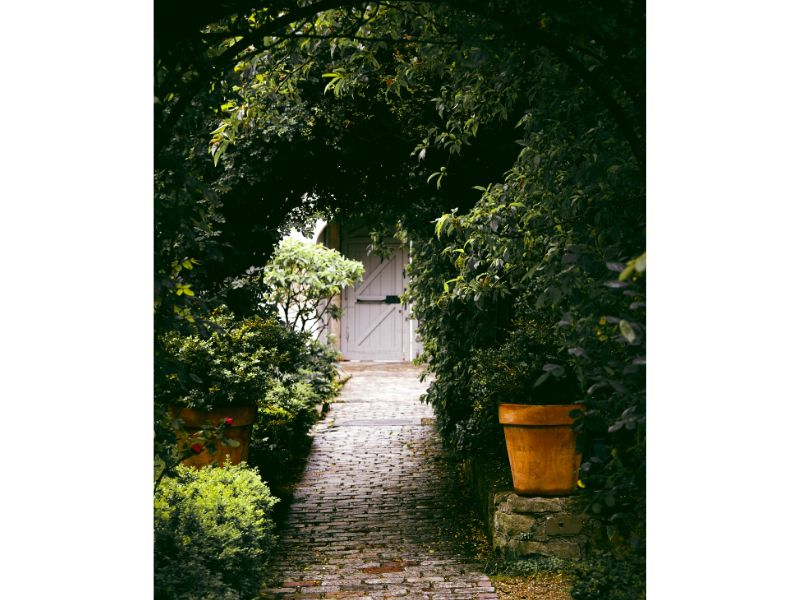 white door-like garden gate set into an ivy clad wall and viewed from the end of a brick path